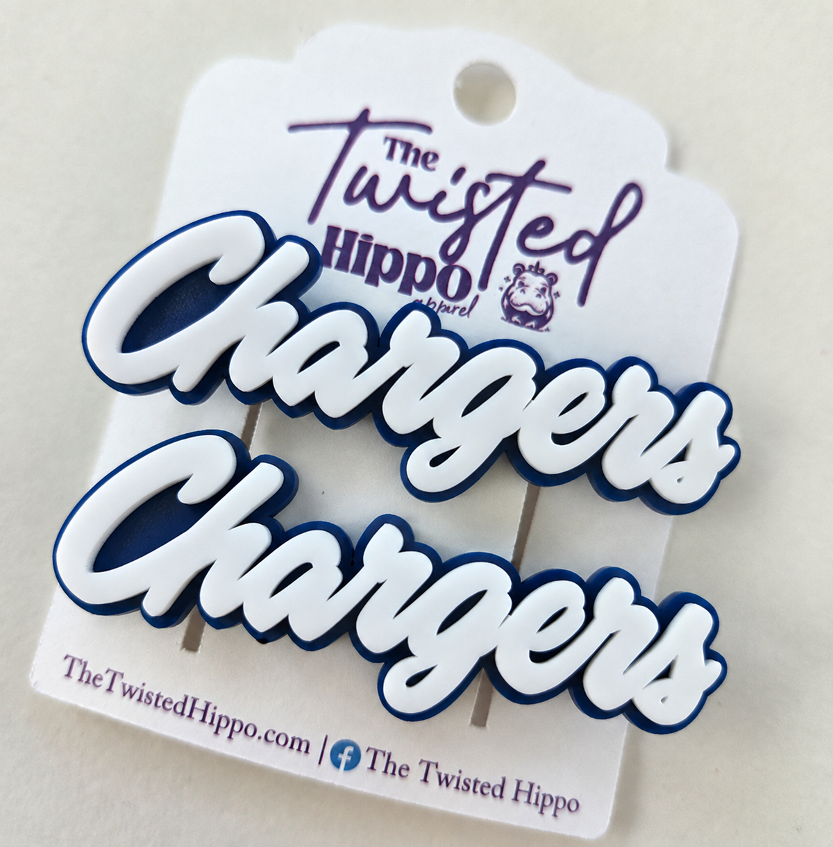 Two matching 'Chargers' script enamel pins in white with dark navy blue outlines, attached to a white branded display card reading 'The Twisted Hippo Brand'.